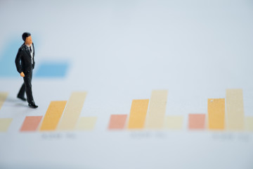 Miniature people businessman walk and analyze bar graph