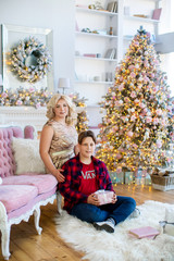 Beautiful mother in luxurious dress and son together in cozy room with Christmas tree and fireplace