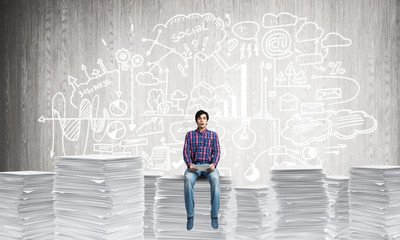 Attractive man sitting on pile of paper documents.