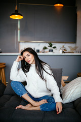 Beautiful girl in a white jacket and jeans is resting on the sofa at home. portrait, scandinavian style