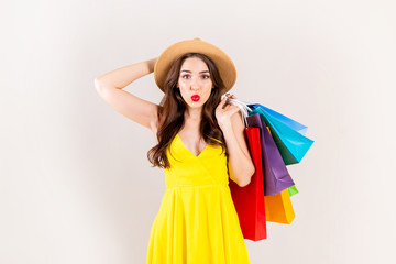 Spring summer season sale concept. Attractive young woman with long brunette hair, wearing sexy yellow dress, holding many different blank shopping bags over white background. Copy space, close up.