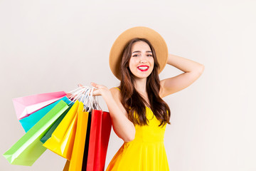 Spring summer season sale concept. Attractive young woman with long brunette hair, wearing sexy yellow dress, holding many different blank shopping bags over white background. Copy space, close up.
