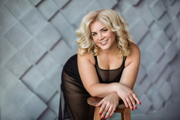 Fototapeta premium Beautiful blonde girl in black dress leaned on chair