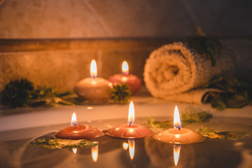relaxing spa background with candles floating in the bath water, some green petals and a towel near the water surface
