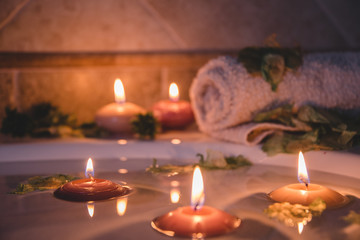 relaxing spa background with candles floating in the bath water, some green petals and a towel near the water surface