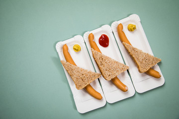 Drei Wiener Würstchen mit Vollkorn Brot Scheibe auf Einweg Pappteller mit Senf und Ketchup auf Hintergrund Grün