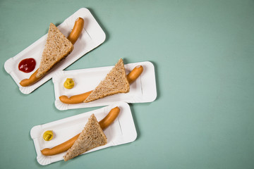 Drei Wiener Würstchen mit Vollkorn Brot Scheibe auf Einweg Pappteller mit Senf und Ketchup auf Hintergrund Grün