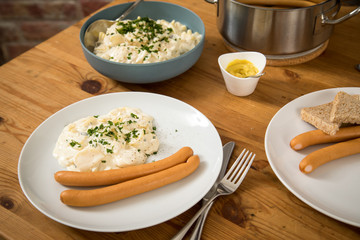 Wiener Würstchen im Topf, Senf und  Norddeutscher Kartoffelsalat mit Mayonnaise, Ei und Gurke als Mahlzeit auf Holz Tisch