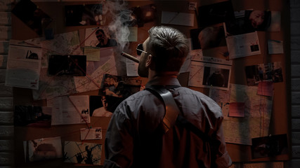 Male cop with cigar analyzing information of crime on investigation board