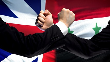 Great Britain vs Syria confrontation, fists on flag background, diplomacy