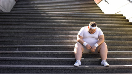 Upset man sitting alone on stairs, fighting with overweight and food addiction - obrazy, fototapety, plakaty
