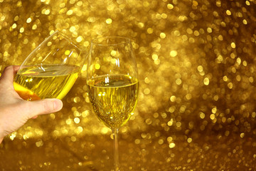 Lampka szampana w dłoni na złotym, błyszczącym tle.