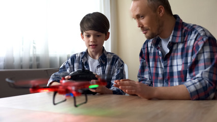 Excited little boy operating new drone model at home, father helping his son