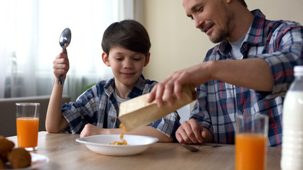 Caring father preparing cornflakes for son in morning, family breakfast at home