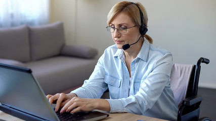 Senior female manager in wheelchair typing on laptop, work for disabled people