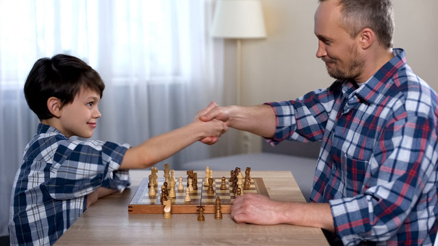 Male kid winning chess with his father, little son shaking hand with dad, hobby