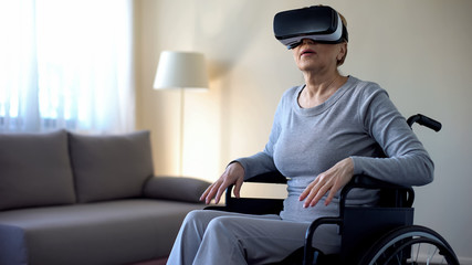 Aged female sitting in wheelchair and wearing virtual reality headset, game