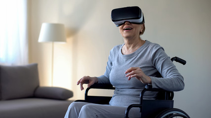 Retired woman in wheelchair wearing vr goggles and enjoying game, technology - Powered by Adobe