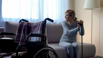 Disabled lady sitting on sofa and looking in window, empty wheelchair in room