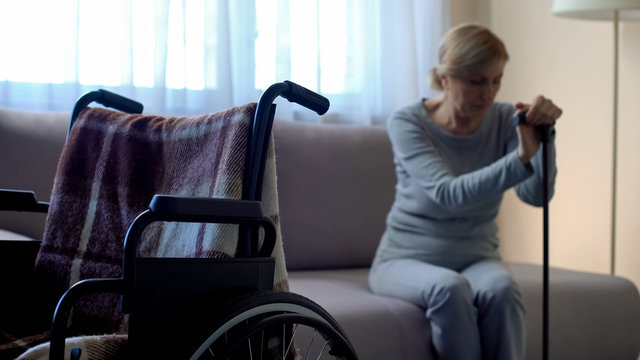 Disabled woman sitting on sofa and crying, empty wheelchair in room, loneliness