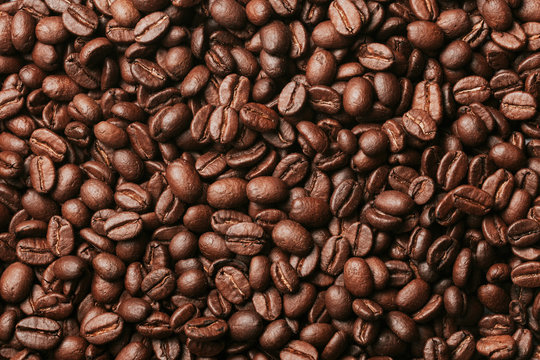 Dark brown roasted coffee seeds artistic pattern background.