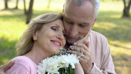 Happy elderly woman holding flowers, stroking male face, mature love, romance