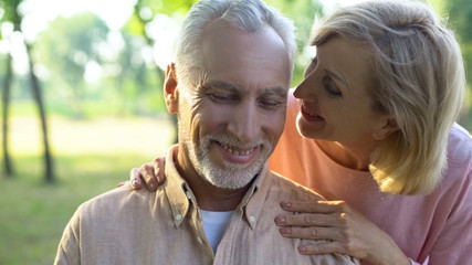Fototapeta premium Caring mature wife flirting with handsome husband in park, whispering compliment