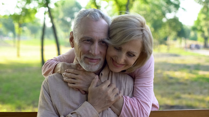 Senior woman hugging husband behind, romantic meeting in park, flirt and fun