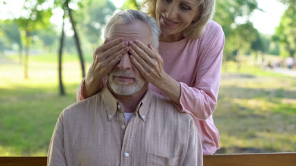 Woman playfully closing husband eyes, meeting outdoors, happiness in old age