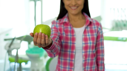 Beautiful girl showing green apple at camera in dental office, healthy teeth