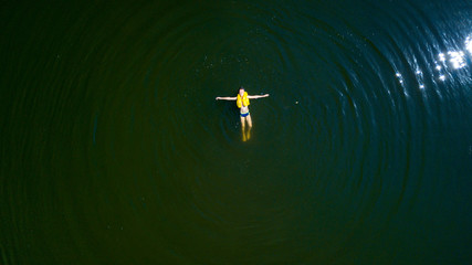 Small boy in yellow life vest bathes on his bach in the river. Kid swims in life-saving jacket in a lake. Aerial view