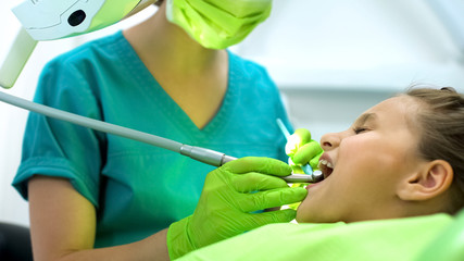 Lady stomatologist polishing little girls tooth enamel, oral cavity protection