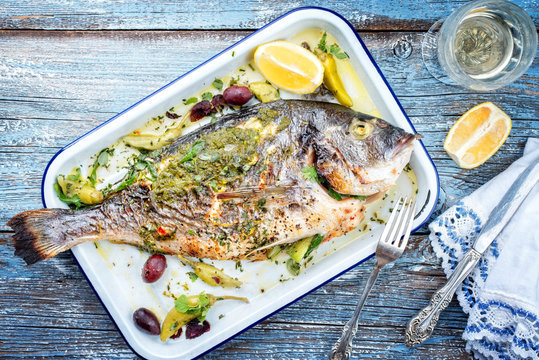Fresh Greek barbecue gilthead seabream with peperoni and Kalamata olives as top view in a white skillet