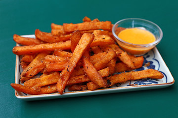 Portion of deep fried sweet potato chips or fries with dipping sauce on plate over table, high angle view - Powered by Adobe