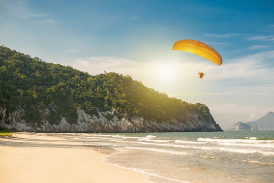 Paramotor is flying over the beach with the sea in the morning,Para motor glider silhouette is flying over beautiful sea with beautiful mountain background at South of Thailand ,copy space.
