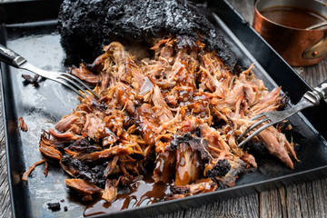 Traditionele barbecue getrokken varkensvlees stuk Bosten kont aan stukken gescheurd met hete saus in braadpan als close-up op een bord