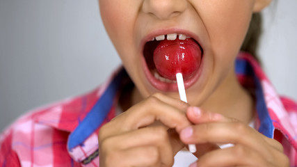 Cute little girl trying to bite lollipop, effect of sugar on teeth, dental care