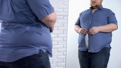 Corpulent man buttoning up tight shirt, oversize clothing problem, appearance