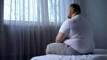 Sad heavy man sitting on bed at home, health problem, depression, insecurities - obrazy, fototapety, plakaty