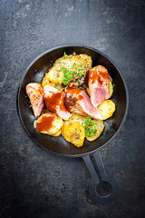 Fried suckling pig fillet with potatoes and hot sauce offered as top view in a modern design cast- iron pan with herbs