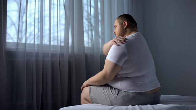 Obese male massaging shoulder muscles, orthopedic and rheumatologic disorders