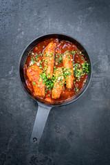 Fried suckling pig fillet in hot tomato chili sauce offered as top view in a modern design cast- iron pan with herbs
