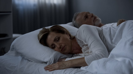 Aging husband and wife lying in bed awake, lady turned back to man, low potency