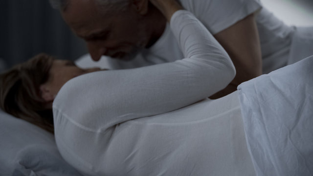 Elderly man caressing woman gently, male and female lying in bed and hugging