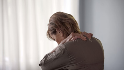 Elderly lady suffering spine ache, standing backwards rubbing neck and shoulders