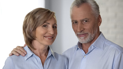 Smiling elderly couple looking at camera, man hugging lady, harmony in relations