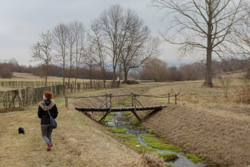 Girl with little dog walk near the river through park in winter without snow