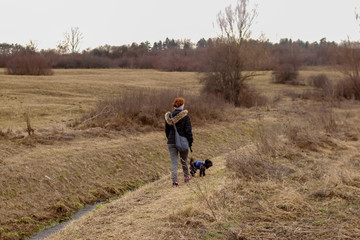 Girl with little dog walk near the river through park in winter without snow