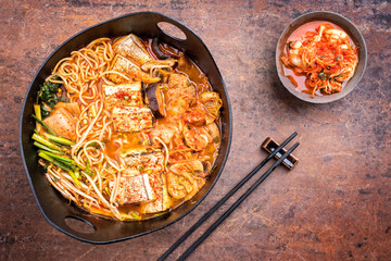Traditional Korean kimchi jjigae with grilled pork belly and ramen as top view in a modern design...