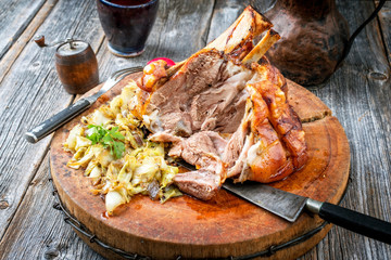 Traditional Bavarian schweinshaxe with coleslaw and preztel as closeup on a wooden cutting board